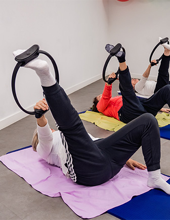 Alumnas tumbadas con la pierna elevada y un aro de pilates en el pie