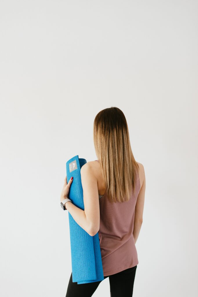 Mujer de espaldas con una esterilla de pilates bajo el brazo